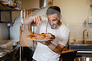 Male chef is sprinkling fresh oregano over a traditionally made home pizza