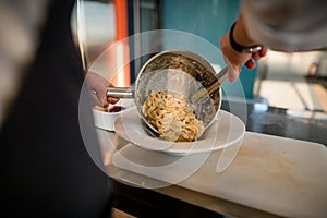 Male chef takes out cooked pasta from pan and puts it in a plate.