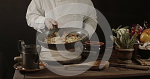 Male chef in white uniform holding a frying pan, sautÃ©ing spaghetti with fresh vegetables