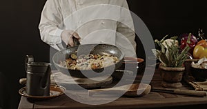 Male chef in white uniform holding a frying pan, sautÃ©ing spaghetti with fresh vegetables