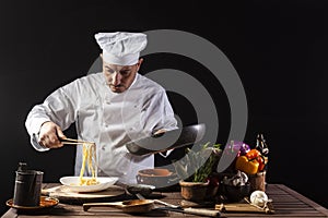 Male chef in white uniform prepares spaghetti with vegetables on the dish