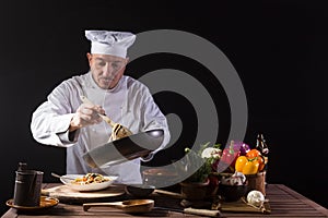 Male chef in white uniform prepares spaghetti with vegetables on the dish