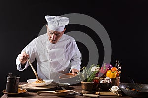 Male chef in white uniform prepares spaghetti with vegetables on the dish