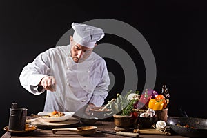 Male chef in white uniform prepares spaghetti with vegetables on the dish