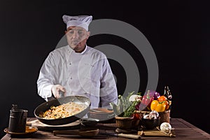 Male chef in white uniform prepares spaghetti with vegetables on the dish