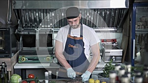 Male chef working in medical mask in kitchen of cafe or restaurant preparing meat for burger during quarantine with