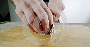 Male cheff hands cutting garlic with a lknife on a wooden cutting board. Close up. Slow motion