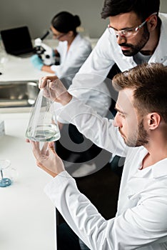 Male chemists in lab coats examining reagent in flask