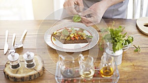 A male chief is adding greenery to a stew salad on a piece of a black bread