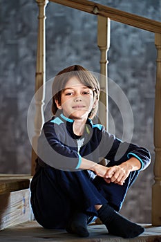 Male child sits on step of wooden staircase between floors.