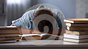 Male child sleeping on table tired of reading books, doing lot of homework
