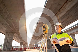 A male civil engineer or surveyor standing holding a blueprint with a happy smile at road construction site, Surveyor equipment.