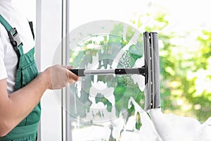 Male cleaner wiping window glass with squeegee indoors