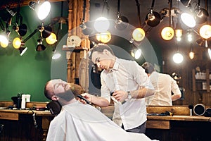 Male client with beard sitting in hairdresser chair. Serious man with long brown beard. Modern popular lumberjack style.