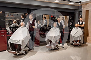 Male clients sitting in hairdresser chairs covered with haircut.