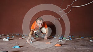 Male climber practicing rock-climbing on a rock wall indoors