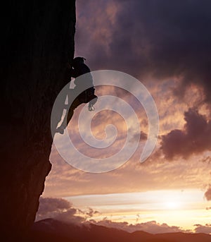 Male silhouette rock climbing, doing next step on cliff. Dark purple cloudy sky on background with copy space. Low angle