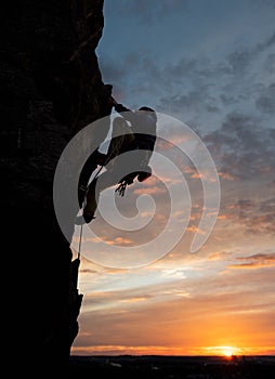 Male climbing looking up taking decisive step on rock. Sky and sunset. Copy space. Rock climbing and leadership concept