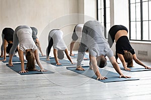 Male coach and group of people performing Downward-facing Dog