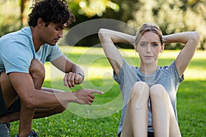 male coach helping young woman exercising in park