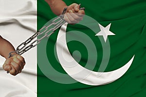 Male coarse hands chained in heavy iron chains against the background of the national flag of Pakistan, the concept of crime in