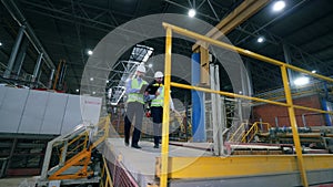 Male colleagues, industrial experts are walking along the modern factory facility.