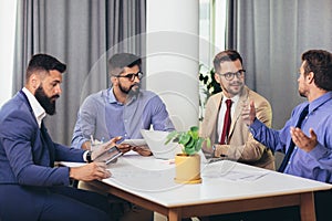 Male colleagues at meeting in office, sitting at table together, sharing ideas