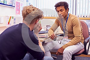 Male College Student Meeting With Campus Counselor Discussing Mental Health Issues photo