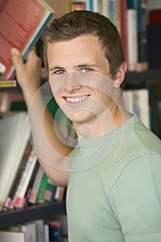 Male college student reaching for a library book