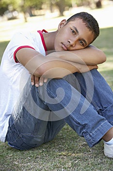 Male College Student Sitting In Park Looking Unhappy
