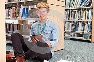 Male College Student Studying In Library With Digital Tablet
