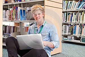 Male College Student Studying In Library With Laptop