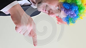 Male comedian in colorful wig pointing finger to side, space for advertisement. Vertical video