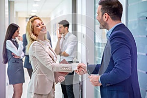 Male company director, greeting attractive blond haired lady to his business team. Handshake and new employee concept.