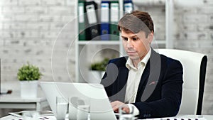 Male confident office worker wearing suit typing on laptop looking at screen at workplace