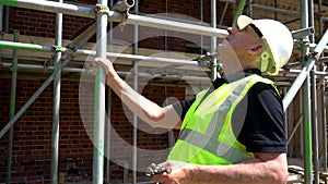 Male construction worker on building site inspecting and checking scaffolding for health and safety