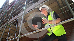 Male construction worker on building site writing on clipboard and talking on cell phone