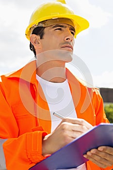 Male construction worker with clipboard looking away outside