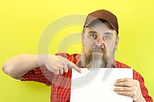 Male construction worker holding blank advertising board. Construction worker with poster. A rude, bearded, stern man in a red shi