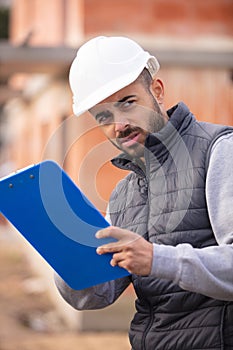 male construction worker outdoors writing on clipboard