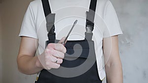 A male construction worker in overalls shows a flat screwdriver to the camera.