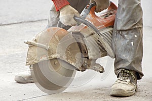 A male construction worker saws asphalt with a seamcutter, dust swirls from under the saw, construction and road work to repair