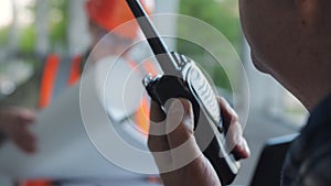 A male construction worker talks on a walkie-talkie with subordinates, while a woman in a construction helmet examines