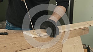 A male construction worker uses a drill to make a hole in a wooden plank.