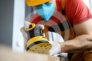 Male construction worker wearing hardhat and protective mask using sanding machine