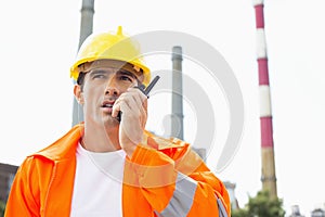 Male construction worker wearing reflective workwear communicating on walkie-talkie at site