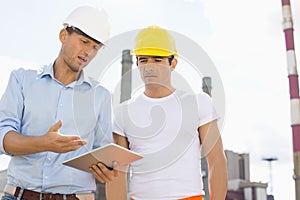 Male construction workers discussing over digital tablet at industry