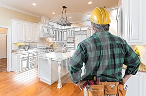 Male Contractor in Hard Hat and Tool Belt Looking At Kitchen Drawing photo