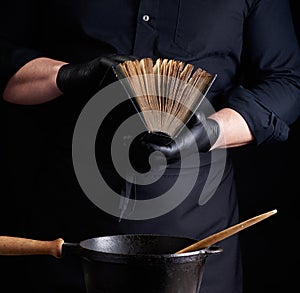 Male cook in a black uniform holds an old cookbook with recipes, on a table is a cast-iron frying pan with a wooden handle