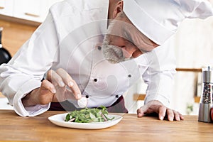 Male cook chef decorating garnishing prepared salad dish on the plate in restaurant commercial kitchen.